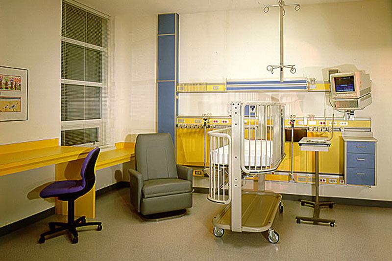 Interior photo of hospital room. Crib bed and chair sit in the middle of the room.